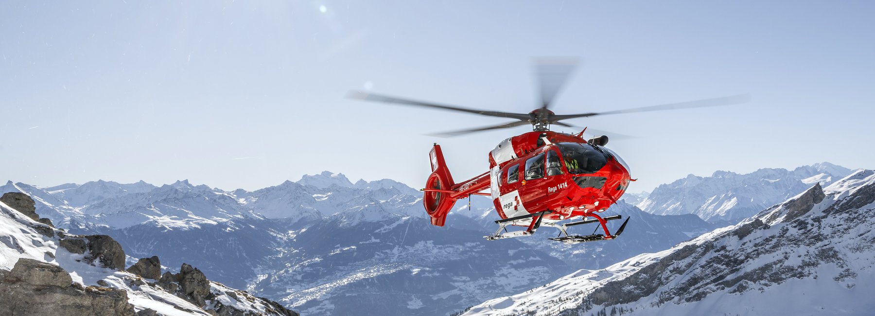 Der Rega-Helikopter fliegt über die Schweizer Schneeberge